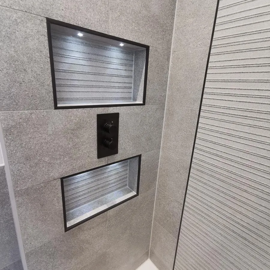 Grey tiled shower wall with two lit recessed niches and a black shower control