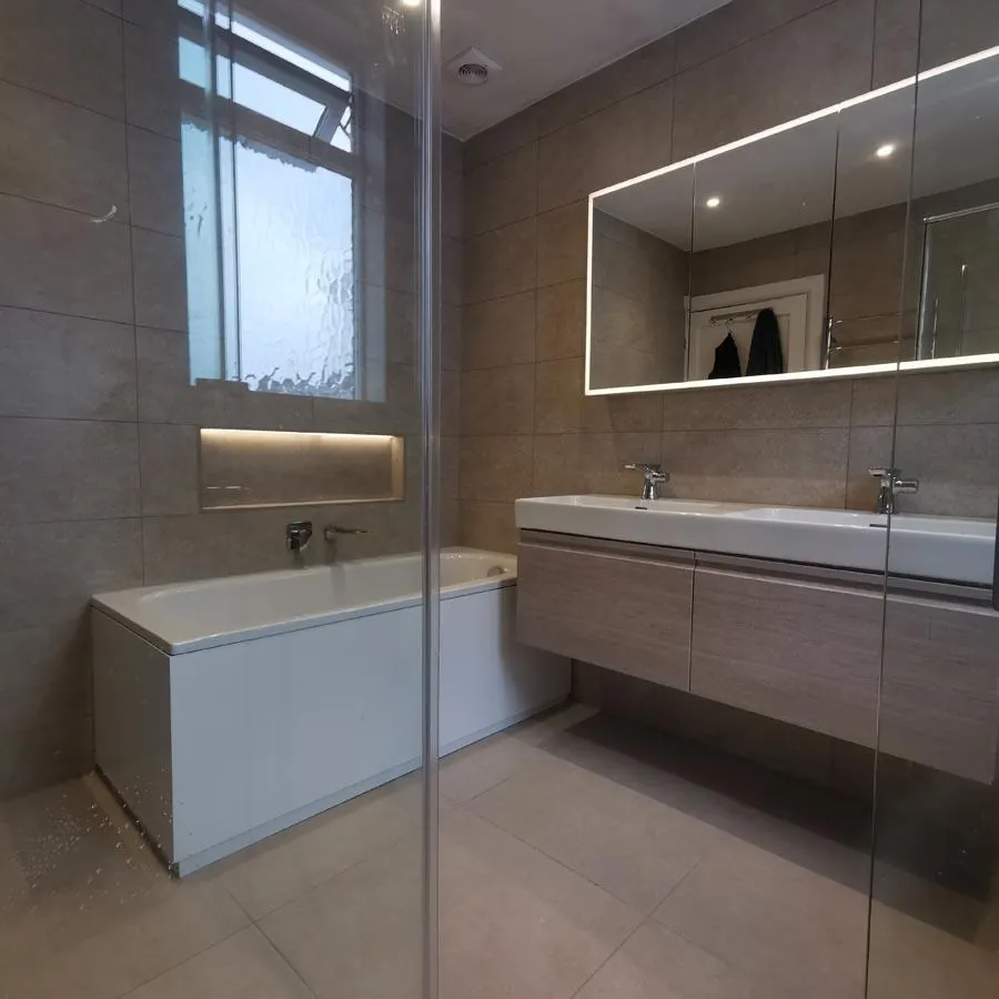 Bathroom with a panelled bath, long wood-effect vanity and large lit mirror