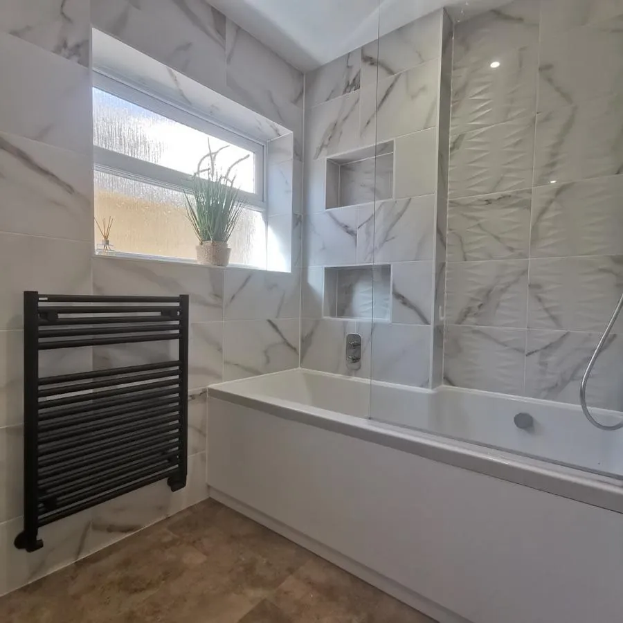 Bathroom with marble-effect tiles, two shower niches, a bath and black towel radiator