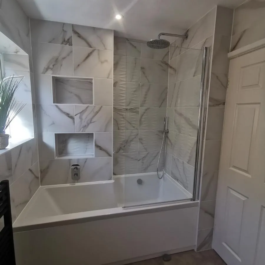 Shower over a bath with marble-effect wall tiles and two tiled niches