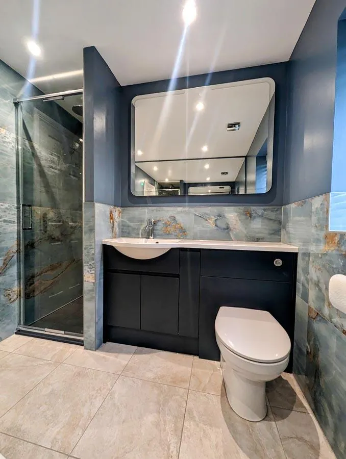 Bathroom with a navy vanity unit, lit mirror and teal tiled wall