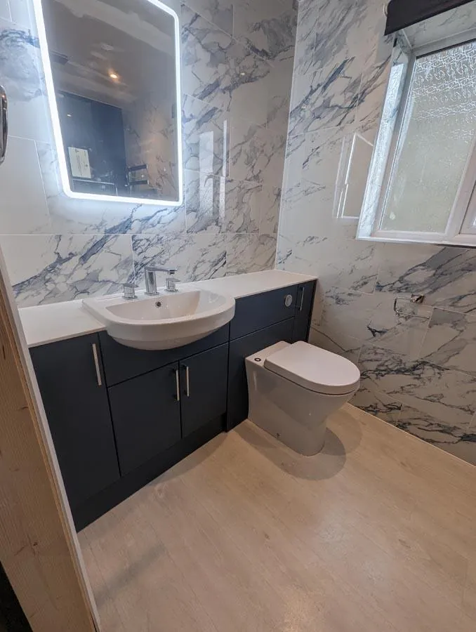 Navy vanity unit with a lit mirror and marble-effect wall tiles