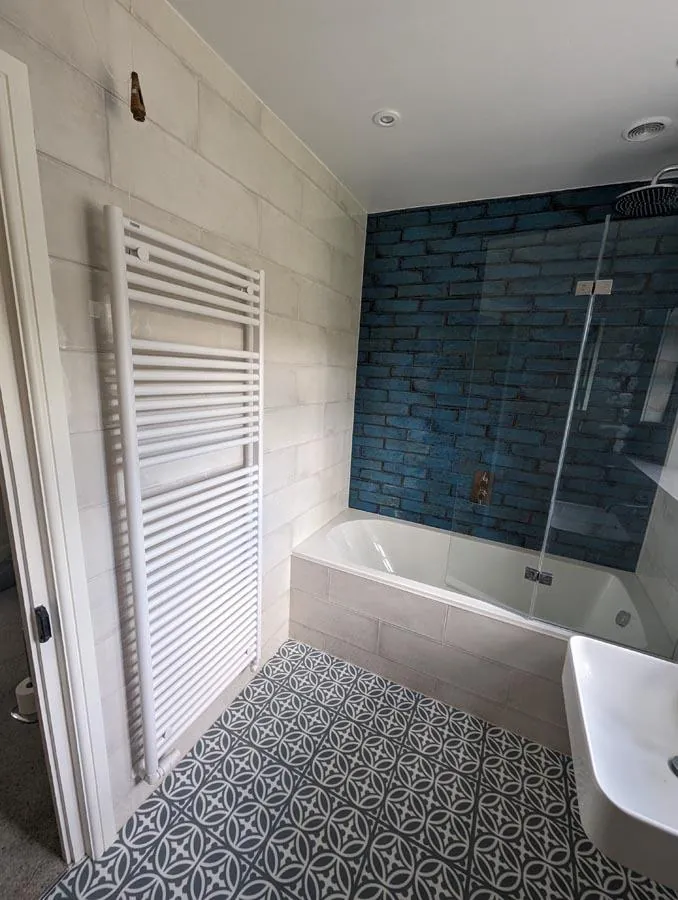 Bath with a glass screen, blue metro tiled wall and patterned floor