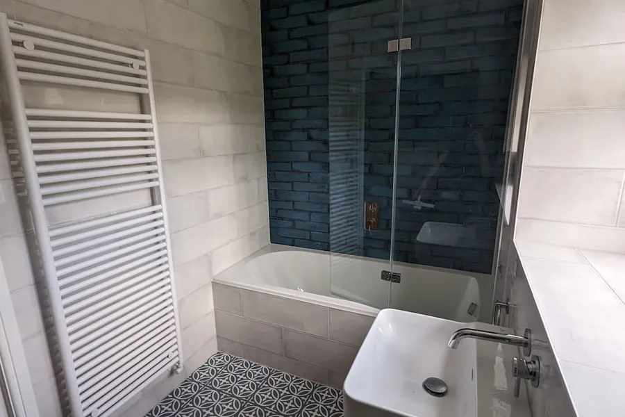 Bath with a glass screen, blue metro tiles and a white towel radiator