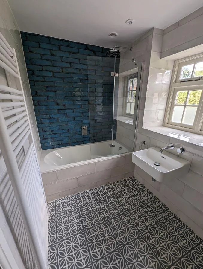 Bathroom with a blue metro tiled bath wall, patterned floor and white radiator