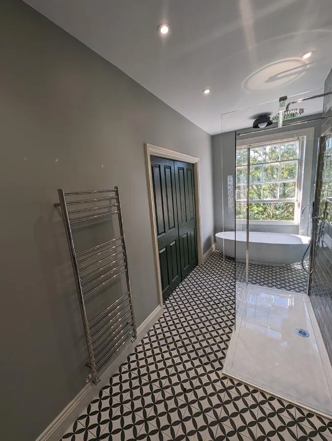 Long bathroom with a geometric tiled floor, chrome towel rail and walk-in shower