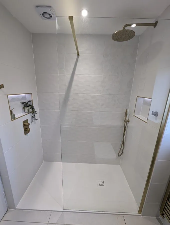 Large walk-in shower with brass fittings and a tiled niche