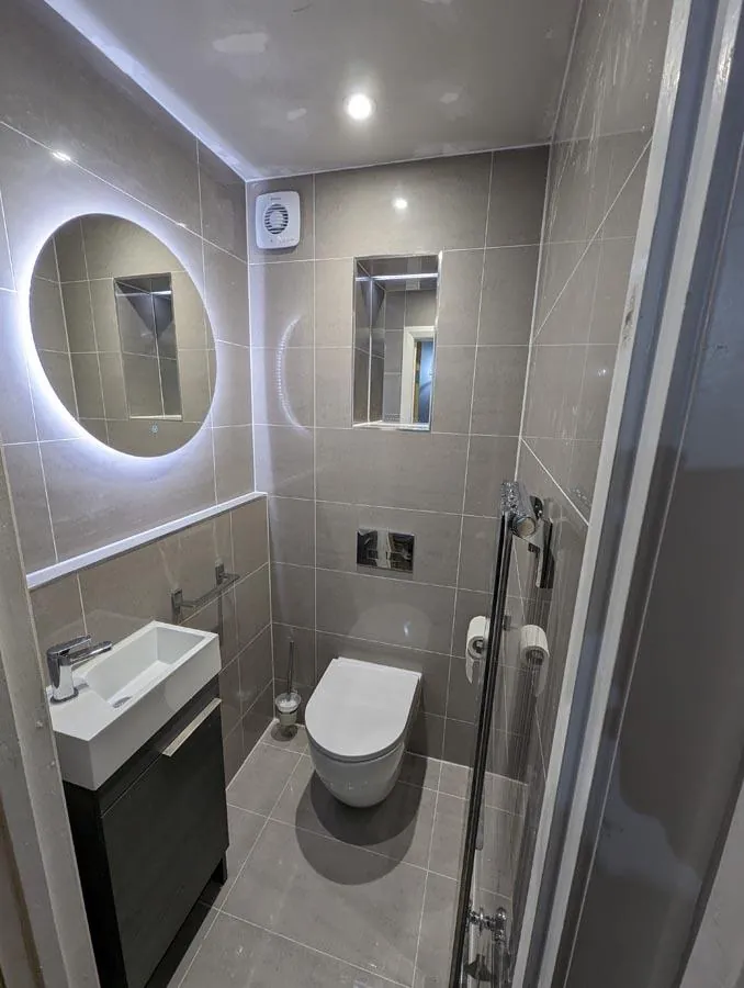 Bathroom with a round lit mirror, wall-hung basin and walk-in shower