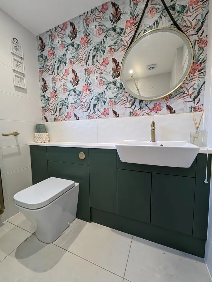 Floral feature wallpaper, a round mirror and a dark green fitted vanity unit